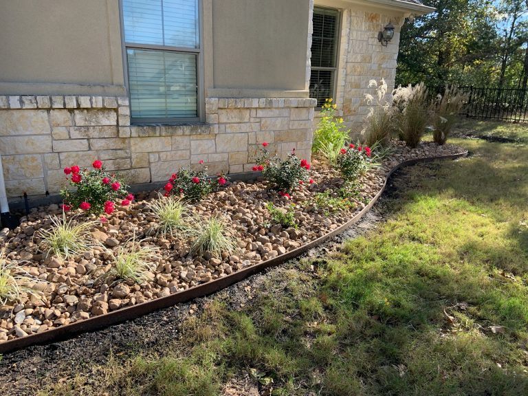 bull rock in landscape bed, native grasses, roses, limestone house siding